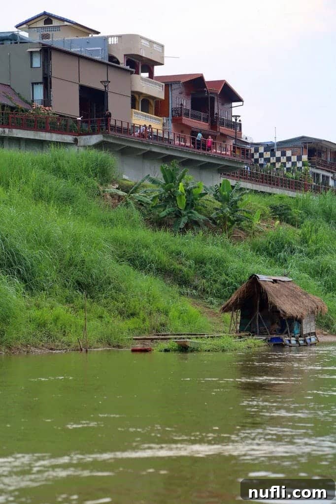 Mighty Mekong Voyage: Thailand to Laos 12 A striking visual contrast of old and new architecture along the Mekong River, showcasing traditional homes beside emerging modern structures in Thailand.