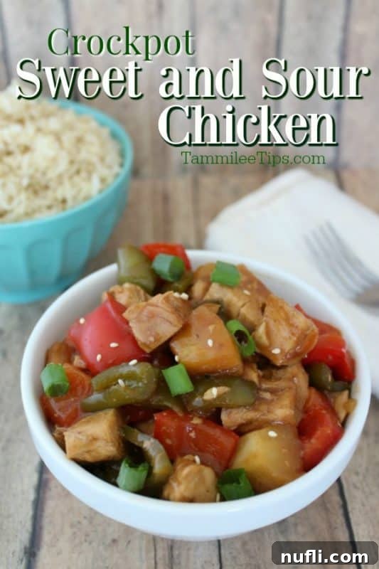 A vibrant bowl of Crockpot Sweet and Sour Chicken, garnished and ready to serve, sits beside a bowl of fluffy white rice, a fork, and a cloth napkin, highlighting its delicious appeal.