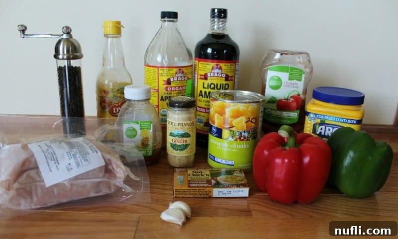 A selection of fresh ingredients for Sweet and Sour Chicken laid out on a rustic wooden counter, including juicy pineapple chunks, vibrant bell peppers, tender chicken breast, aromatic garlic, ground ginger, cornstarch for thickening, a bottle of soy sauce, sweet honey, and tangy apple cider vinegar.