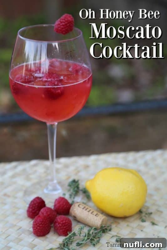 Oh Honey Bee Moscato Cocktail next to a wine glass, lemon, and raspberries