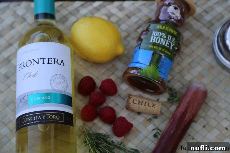 Moscato wine, raspberries, honey, a lemon, and a muddler on a placemat