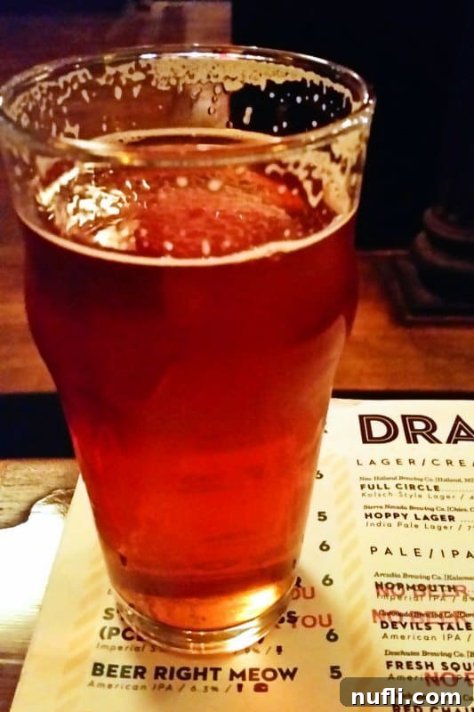 Glass of craft beer resting on a menu at HopCat, featuring their famous Crack Fries