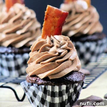 A close-up of a Double Chocolate Bacon Cupcake with a paper liner, showcasing rich chocolate frosting and crispy bacon garnish.