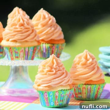 Close-up of a beautifully frosted Orange Julius cupcake in a paper wrapper, sitting on an elegant cake stand.
