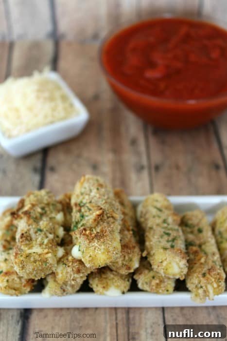 Crispy homemade baked mozzarella sticks on a white platter, served with a bowl of marinara sauce and fresh parmesan cheese.