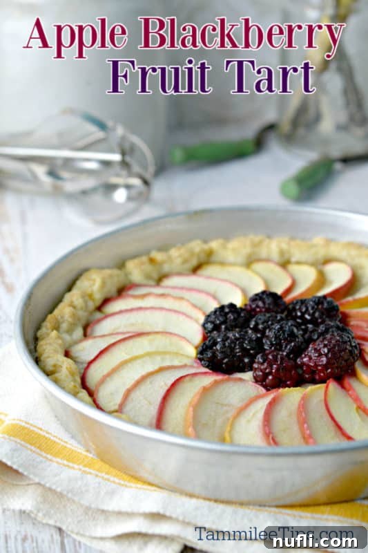 Vibrant Apple Blackberry Fruit Tart glistening with fruit filling in a classic tart pan, set on a textured cloth napkin.