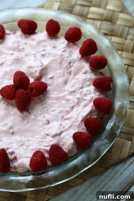 A vibrant no-bake raspberry pie set in a glass pie pan on a rustic placemat, ready to be chilled