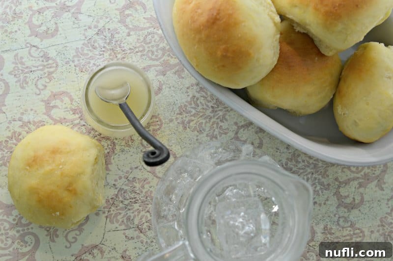 A glass jar filled with golden lemon butter, sitting next to a small bowl of dinner rolls.
