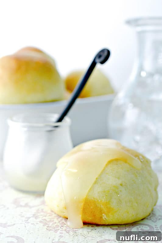Lemon butter on top of a roll next to a jar with a spoon in it and a bowl of rolls