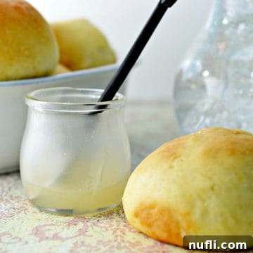 Lemon butter in a glass jar next to a roll with a bowl of rolls in the background.