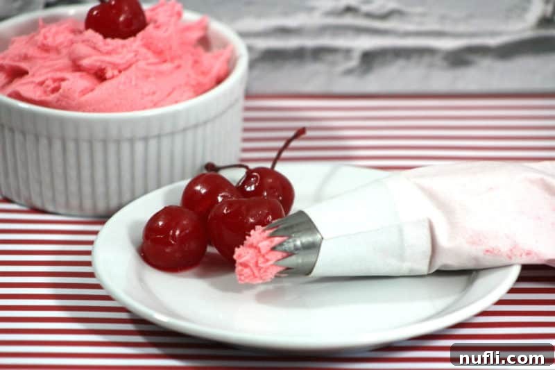 Close-up of fluffy cherry frosting in a white bowl next to a plate with bright red maraschino cherries and an icing dispenser, ready for decorating.