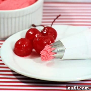 Beautifully piped cherry frosting on a white plate, garnished with glistening maraschino cherries.