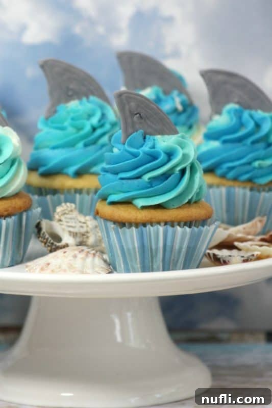 Delicious shark fin cupcakes on a white cake stand, perfect for Shark Week celebrations or ocean-themed parties.