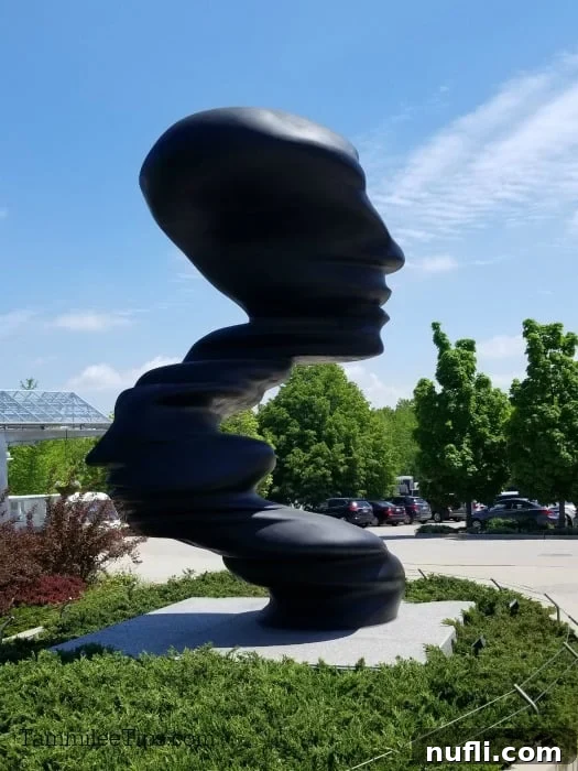 Meijer Gardens Grand Rapids Art and Nature Escape 2 Large, curving bronze sculpture, 'Bent of Mind,' by Tony Cragg, with cars and trees in the background