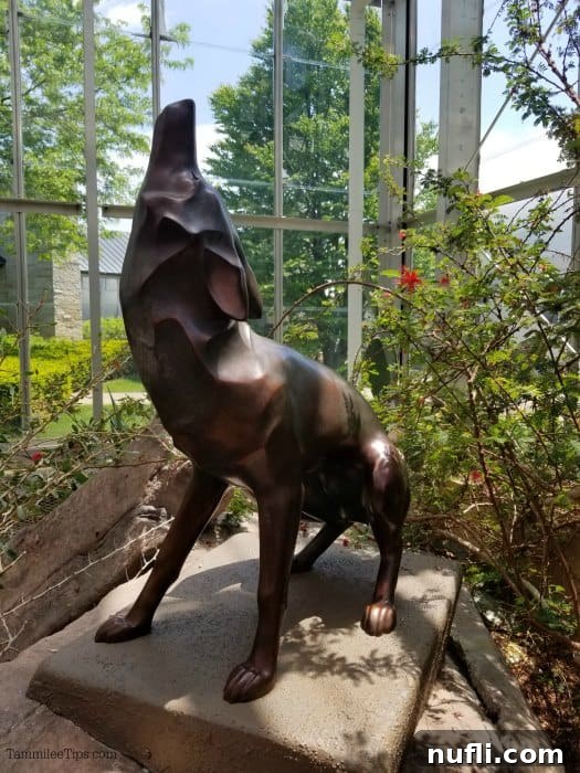 Meijer Gardens Grand Rapids Art and Nature Escape 3 Coyote statue with a detailed, textured surface inside a glass conservatory, surrounded by lush green plants.
