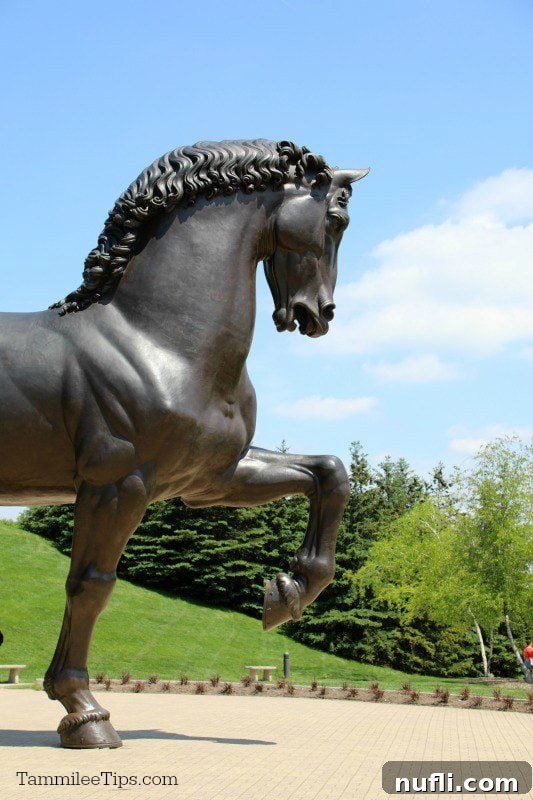 Meijer Gardens Grand Rapids Art and Nature Escape 6 Massive bronze horse sculpture, 'American Horse,' with one leg lifted, standing on a grassy hill with trees in the background.