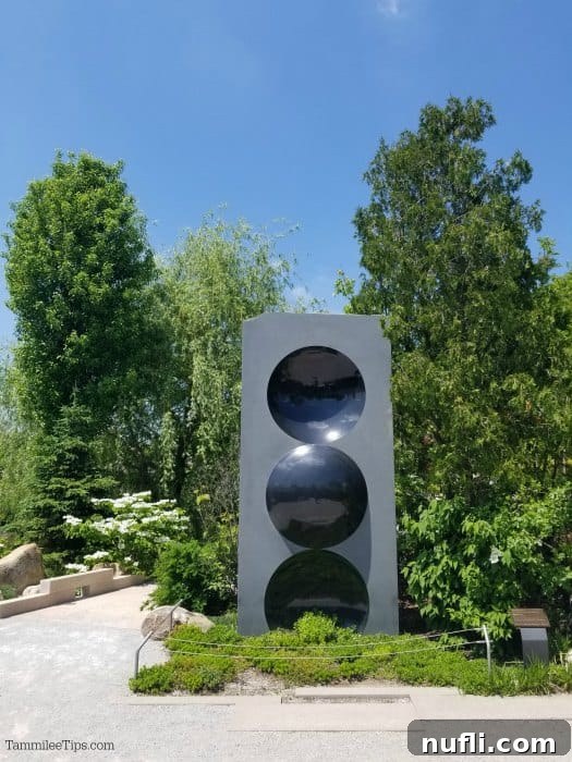 Meijer Gardens Grand Rapids Art and Nature Escape 10 Abstract sculpture 'Untitled' by Anish Kapoor, featuring black spheres atop a grey monument, with trees in the soft focus background.