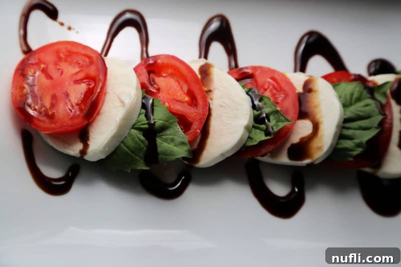 Simple & Irresistible Caprese Salad 4 caprese salad with tomato slices, mozzarella, and basil with a drizzle of balsamic glaze on a white platter