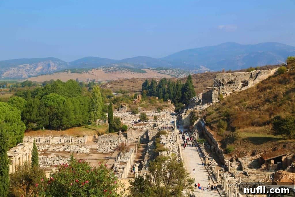 A panoramic view looking down on the main thoroughfare of Ephesus, bustling with tourists exploring the ruins.