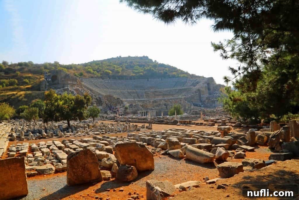A sweeping view of the vast Great Theater of Ephesus, with broken stone fragments in the foreground.