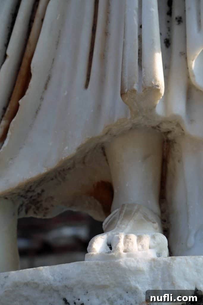 A detailed shot of an ancient statue's foot and draped robes in Ephesus, highlighting the artistry.