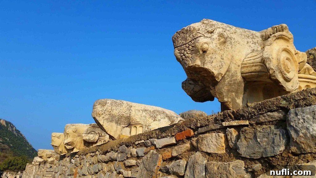 Broken fragments of sculptures and architectural elements neatly arranged against a rock wall in Ephesus.