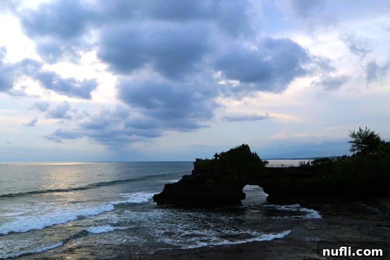 Tanah Lot Temple at dusk, beautifully illuminated over the water on a cloudy evening