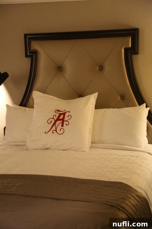 A pristine queen-size bed with crisp white linens and a decorative pillow adorned with the letter 'A' at The Algonquin Resort, inviting ultimate relaxation.