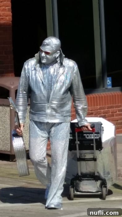 A street performer dressed in all silver with sunglasses and a guitar entertaining crowds during the Buskers on the Bay Festival.