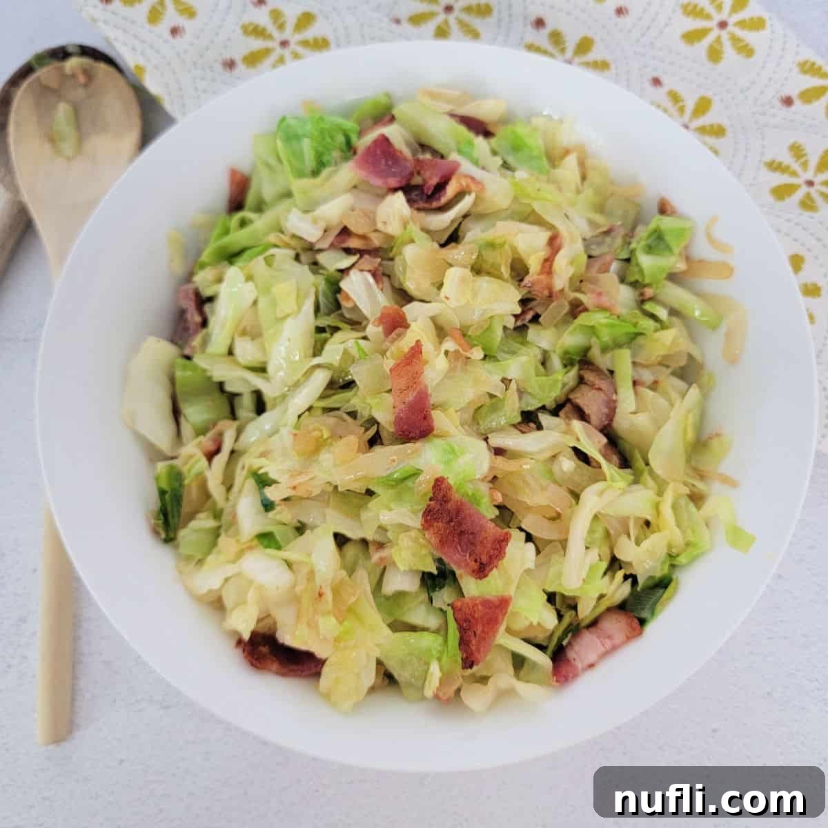 Southern fried cabbage with bacon in a white bowl next to a wooden spoon