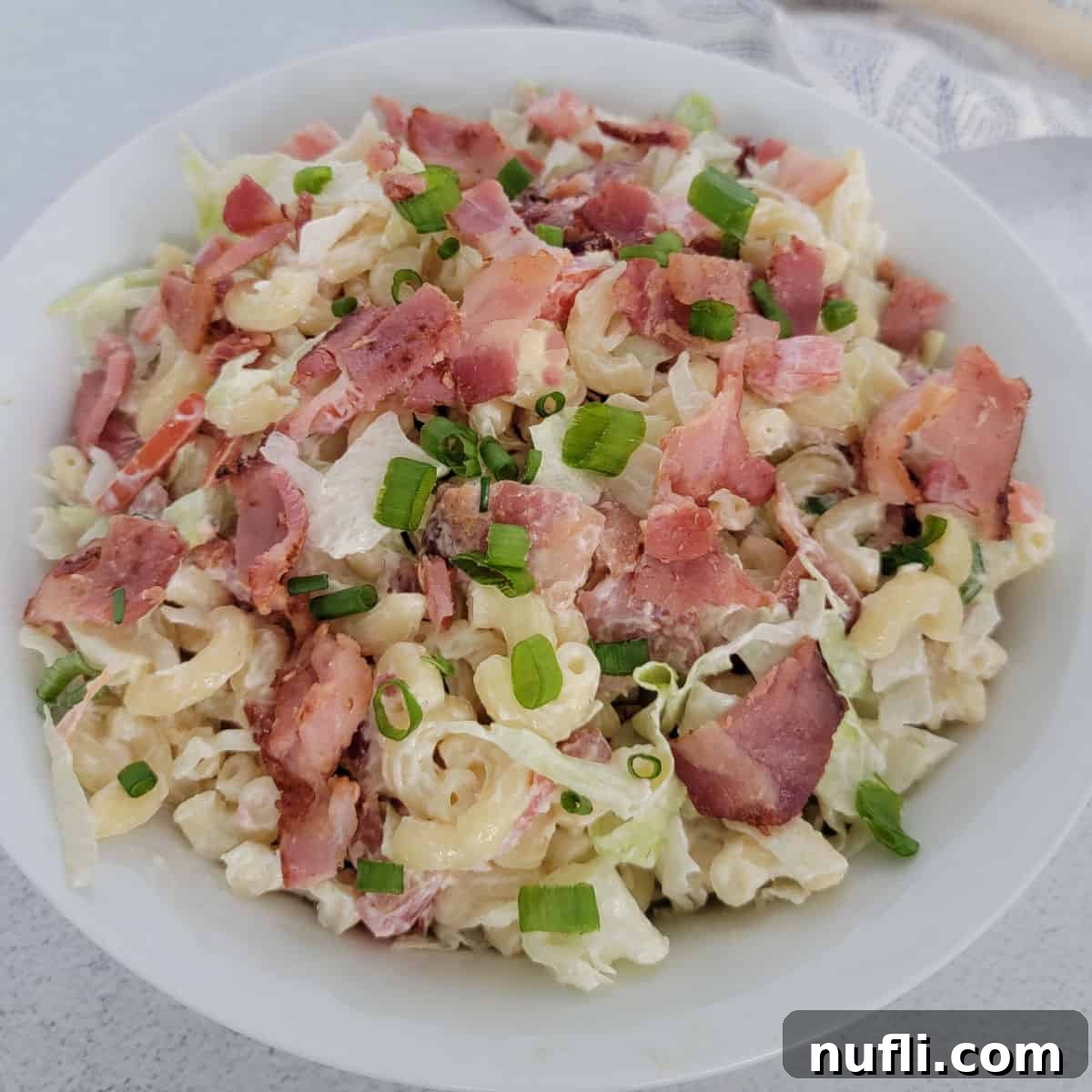 BLT pasta salad garnished with green onion in a white bowl